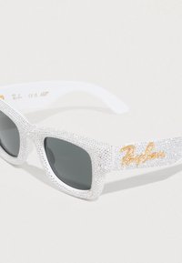 Λευκά γυαλιά ηλίου Ray-Ban με σκούρους φακούς, καλυμμένα ολόκληρα με μικρές καθαρές στρας, και χρυσό λογότυπο Ray-Ban στον βραχίονα.