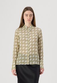 Camicia a maniche lunghe con bottoni realizzata in un tessuto leggero. Presenta una stampa geometrica ripetitiva in verde e marrone su sfondo crema.