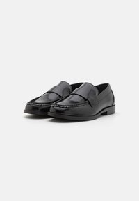 Sorte skinnloafers med en glatt finish, med en bred stropp over vristen og en sydd detalj langs sålen.