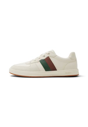 Zapatilla baja de color crema con franjas laterales marrones y verdes, cordones blancos y una suela de goma marrón clara.