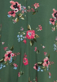 Tecido com padrão floral apresentando grandes flores cor-de-rosa e vermelhas sobre um fundo verde. Textura suave com detalhes intrincados e costura.