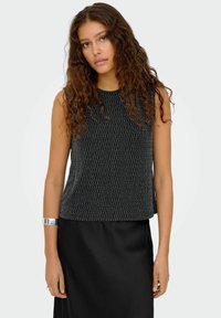 Czarny bezrękawnik z teksturowanym wzorem w zygzak, wykonany z lekkiego materiału, połączony z gładką czarną spódnicą i srebrną bransoletką.