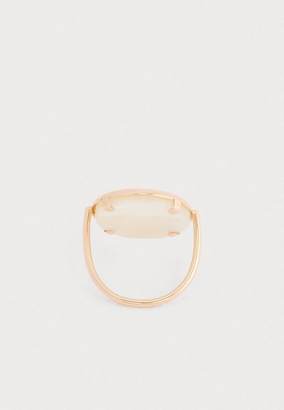 Anel em tom de ouro com uma pedra oval e translúcida, montada numa faixa minimalista com um design aberto. Textura suave, estética moderna.
