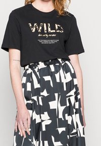 Camiseta negra con la palabra "WILD" en print animal y texto abajo, combinada con una falda fluida con patrones abstractos en blanco sobre un fondo oscuro.