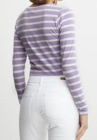 Långärmad lila och vit randig skjorta i kombination med vita jeans, med rundad halsringning och figurnära silhuett.