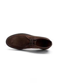 Zapato de hombre en ante marrón con cordones y suela negra, visto desde arriba, aislado sobre fondo blanco.