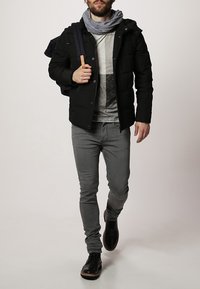 Czarna kurtka puchowa, szara koszulka w paski, szare dopasowane dżinsy i czarne buty. Model nosi niebieski plecak, owinięty w jasnoszary szalik.