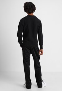 Felpa nera con scollo rotondo, abbinata a pantaloni sportivi neri con zip laterali e dettagli bianchi, entrambi realizzati in tessuto liscio.