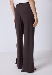 Bruine geribbelde wijde broek met een hoge taille en zijsplitten aan de zoom, gemaakt van zachte stof. Het ontwerp heeft een gladde textuur.