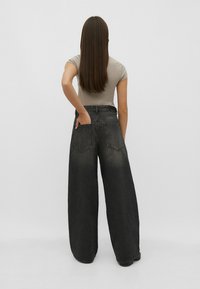 Wide-leg black denim jeans with faded detailing, worn with a fitted gray top. The back features two patch pockets and a high waist design.