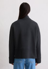 Czarny, oversize sweter z wysokim kołnierzem i ściągaczami, charakteryzujący się gładką fakturą i skróconym dołem, zestawiony z niebieskimi dżinsami.