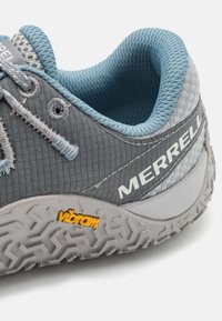 Szare buty sportowe z teksturowaną cholewką, niebieskimi akcentami i charakterystyczną podeszwą Vibram z geometrycznym wzorem bieżnika.