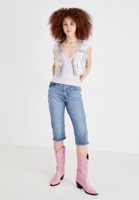 Fémes ezüst színű cropped mellény egy világoslila felsőn, térd fölé érő kék farmerral és hegyes orrú rózsaszín cowboy csizmával párosítva.