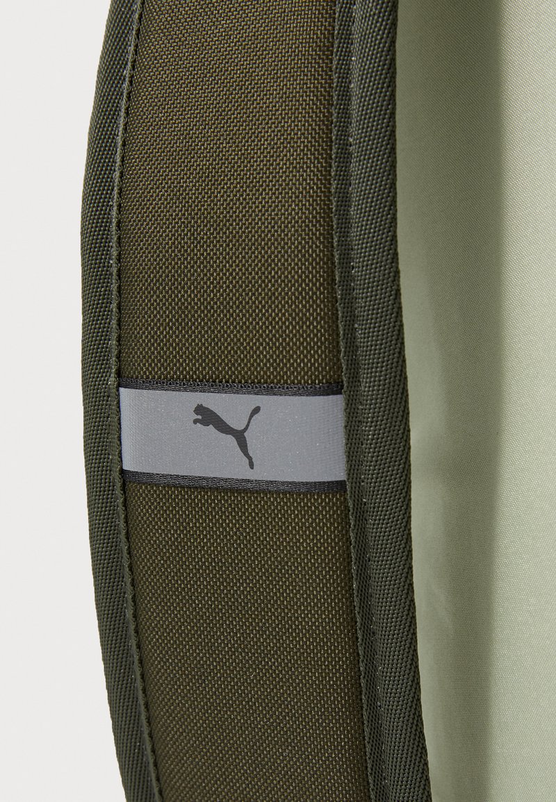 Sac à dos en tissu vert avec des finitions noires ; présente un patch de logo Puma gris. Matériau extérieur texturé avec une doublure intérieure lisse.