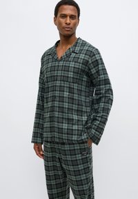 Set di pigiama a quadri verdi e neri realizzato in tessuto morbido; comprende una camicia con bottoni e una tasca, e pantaloni dalla vestibilità ampia.