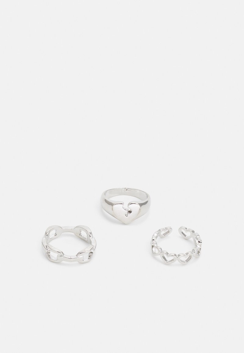 Ensemble de trois anneaux en argent : un rond avec une découpe en forme de cœur, un style maillon de chaîne avec des cœurs, et un design ouvert avec des accents en forme de cœur.