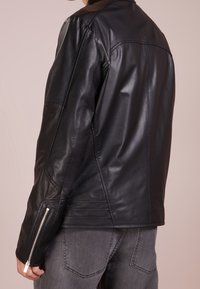 Schwarze Lederjacke mit glatter Textur und tailliertem Design. Verfügt über Reißverschlussmanschetten und Paneeldetails an den Ärmeln und auf dem Rücken.