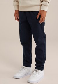 Mörkblå byxor i texturerat tyg, med rak passform och sidofickor, kombinerade med vita sneakers.