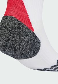 Sportske čarape s bijelom podlogom i crvenim i crnim uzorkom na peti. Deo pete je teksturiran i pretežno sivi.