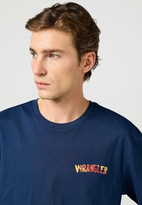 Mörkblå t-shirt i mjukt tyg, med rund halsringning och en färgglad "WRANGLER" logotyp på vänster bröst.