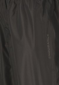 Sort stof close-up med subtile syningsdetaljer og ordet "ENDURANCE" trykt vertikalt i gråt.