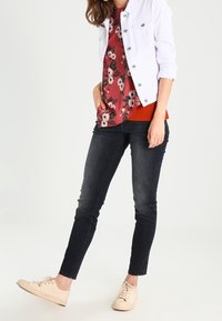 Giacca di jeans bianca, blusa rossa a fiori, sotto giacca arancione, jeans scuri e sneaker beige. Tessuto liscio, design aderente e motivi delicati.