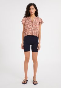 Floral-patterned, short-sleeve, rust-colored top with a v-neckline paired with navy, knee-length shorts and black flip-flop sandals.