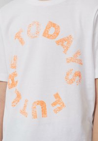 Weißes Baumwoll-T-Shirt mit einem runden orangen Druck, auf dem der Text "DIE ZUKUNFT VON MORGEN" in einer abgenutzten Schriftart steht. Kurze Ärmel und lockere Passform.