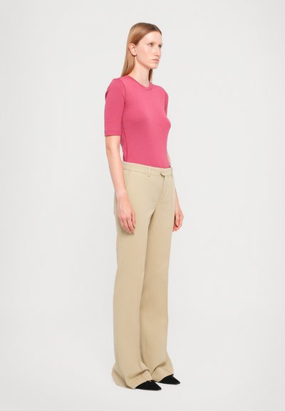 Top rosa ajustado de manga corta combinado con pantalones beige de pierna ancha, que presentan una textura suave y un diseño entallado. Los zapatos negros completan el atuendo.