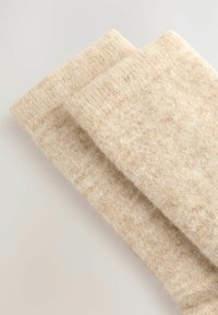 Beige Wollsocken mit einer weichen, strukturierten Oberfläche, ausgestattet mit gerippten Bündchen und einem nahtlosen Design. Zwei Paare sind übereinander gestapelt.