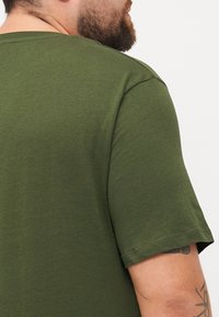 Olijfgroen T-shirt met korte mouwen, gemaakt van zachte katoen. Beschikt over een ronde hals en een ontspannen pasvorm, met een gladde, gelijkmatige textuur.