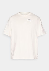 T-shirt z bawełny w kolorze ecru, z krótkim rękawem, okrągłym dekoltem oraz niebieskim nadrukiem "CFC" i logo Nike na klatce piersiowej.