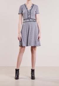 Zwart-wit patroon jurk met een V-hals, korte mouwen en een getailleerde taille, die uitloopt in een rok. Gecombineerd met zwarte enkellaarsjes.