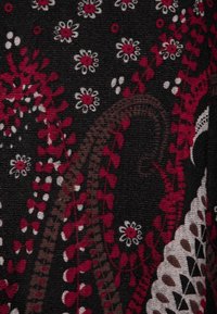 Tissu avec un fond noir orné de motifs paisley et floraux complexes en rouge, blanc et marron. Texture douce, design détaillé.