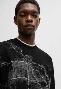 Black sweatshirt featuring a white urban map graphic. The fabric appears soft with a crew neck design and subtle texture.