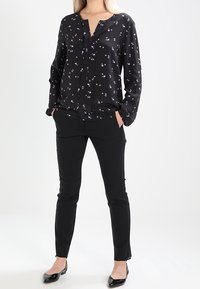 Černá blůza s dlouhým rukávem a malými květinovými vzory, spárovaná s černými upnutými kalhotami a černými balerínami. Hladká tkanina a uvolněný střih.