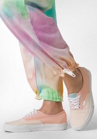 Lyserøde og beige low-top sneakers med hvide snørebånd, sammen med farverige, tie-dye joggers med en snor i cuffen.