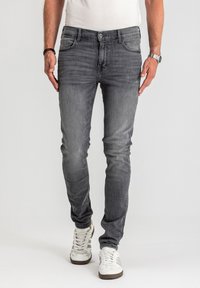 Szare, dopasowane dżinsy o wąskim kroju z efektownym, wyblakłym praniem i pięcioma kieszeniami, zestawione z białymi tenisówkami, charakteryzujące się płaskim przodem i prostym krojem nogawek.