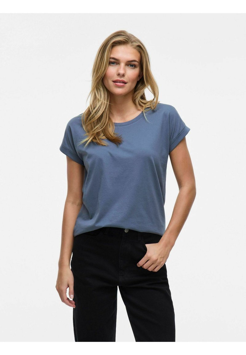 Blå bomulls-t-shirt med upprullade korta ärmar och rund halsringning, i kombination med svarta jeans. Slät textur, avslappnad passform.