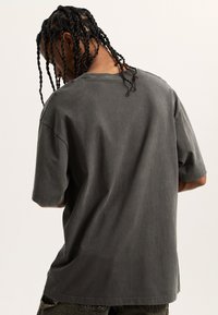 Přetáhnuté tričko s krátkým rukávem vyrobené z bavlny, v tlumené šedé barvě. Má jednoduchý kulatý výstřih a volný střih.