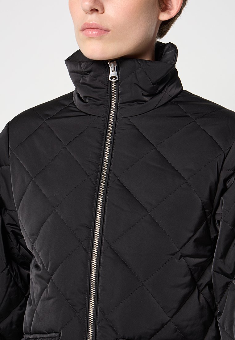 Zwarte gewatteerde jas met een hoge kraag, ritssluiting en geometrisch diamanten patroon. Zachte textuur, ontworpen voor warmte en comfort.