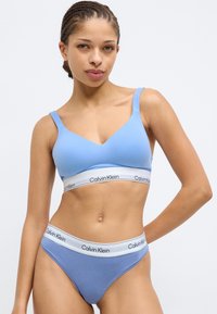 Γαλάζιο σουτιέν Calvin Klein με v-λαιμόκοψη, διαθέτοντας φαρδιές τιράντες και φαρδύ ελαστικό με αντίθετο λογότυπο στη μέση. Ομαλή υφή υφάσματος.