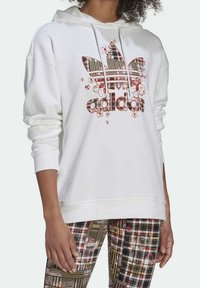 Vit huvtröja med en flerfärgad rutig Adidas-logotyp med blommiga detaljer. Kombinerad med mönstrade leggings i liknande nyanser och texturer.