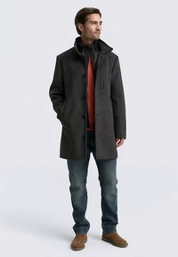 Grå kappa i ullblandning med en strukturerad krage, knappstängning och sidofickor; lager-på-lager över en röd tröja och kombinerad med blå jeans.