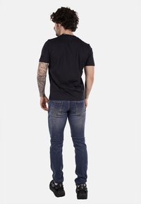 Camiseta negra de manga corta, jeans ajustados azules y zapatillas negras. La camiseta tiene un escote redondo; los jeans cuentan con bolsillos traseros y un ligero desgastado.