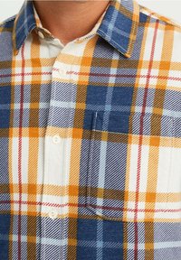 Chemise à boutons à carreaux orange, bleu et blanc. Tissu doux, poche poitrine unique et col standard.