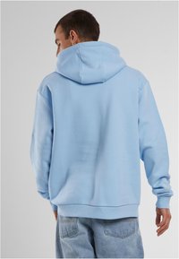 Svijetloplava dukserica s kenguruvim džepom i podesivom kapuljačom. Mekani materijal, rebrasti manžeti i pojas, nosi se s svijetloplavim trapericama.