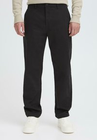 Black cotton chinos with a relaxed fit, featuring a button closure, side pockets, and tapering at the ankles, paired with white sneakers.