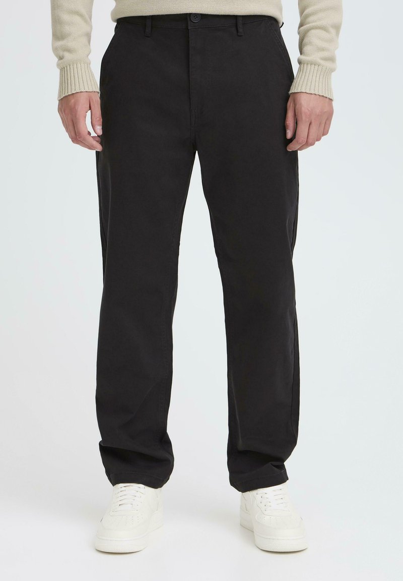 Black cotton chinos with a relaxed fit, featuring a button closure, side pockets, and tapering at the ankles, paired with white sneakers.