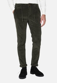 Pantaloni in corduroy verde oliva con una vestibilità affusolata, vita con cordoncino e tasche anteriori, abbinati a stivaletti neri alla caviglia.